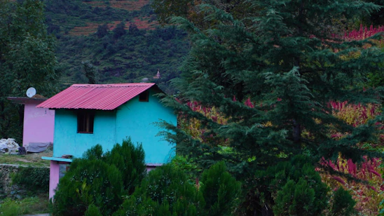 A cozy turquoise-themed homestay surrounded by lush gardens under a vibrant rainbow sky at sunset.