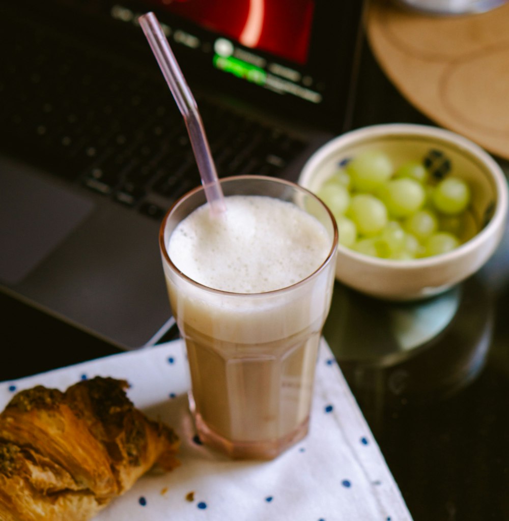 a glass of milk next to a croissant and a bowl of grapes