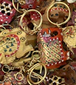 A collection of intricately painted wooden keychains with animal motifs, featuring vibrant colors and detailed patterns. The keychains include designs of animals with playful expressions, surrounded by gold rings and chains.