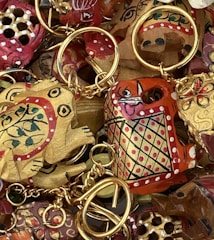 A collection of intricately painted wooden keychains with animal motifs, featuring vibrant colors and detailed patterns. The keychains include designs of animals with playful expressions, surrounded by gold rings and chains.