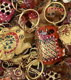A collection of intricately painted wooden keychains with animal motifs, featuring vibrant colors and detailed patterns. The keychains include designs of animals with playful expressions, surrounded by gold rings and chains.