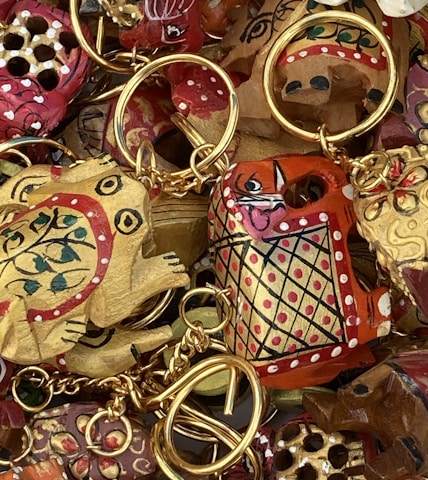 A collection of intricately painted wooden keychains with animal motifs, featuring vibrant colors and detailed patterns. The keychains include designs of animals with playful expressions, surrounded by gold rings and chains.