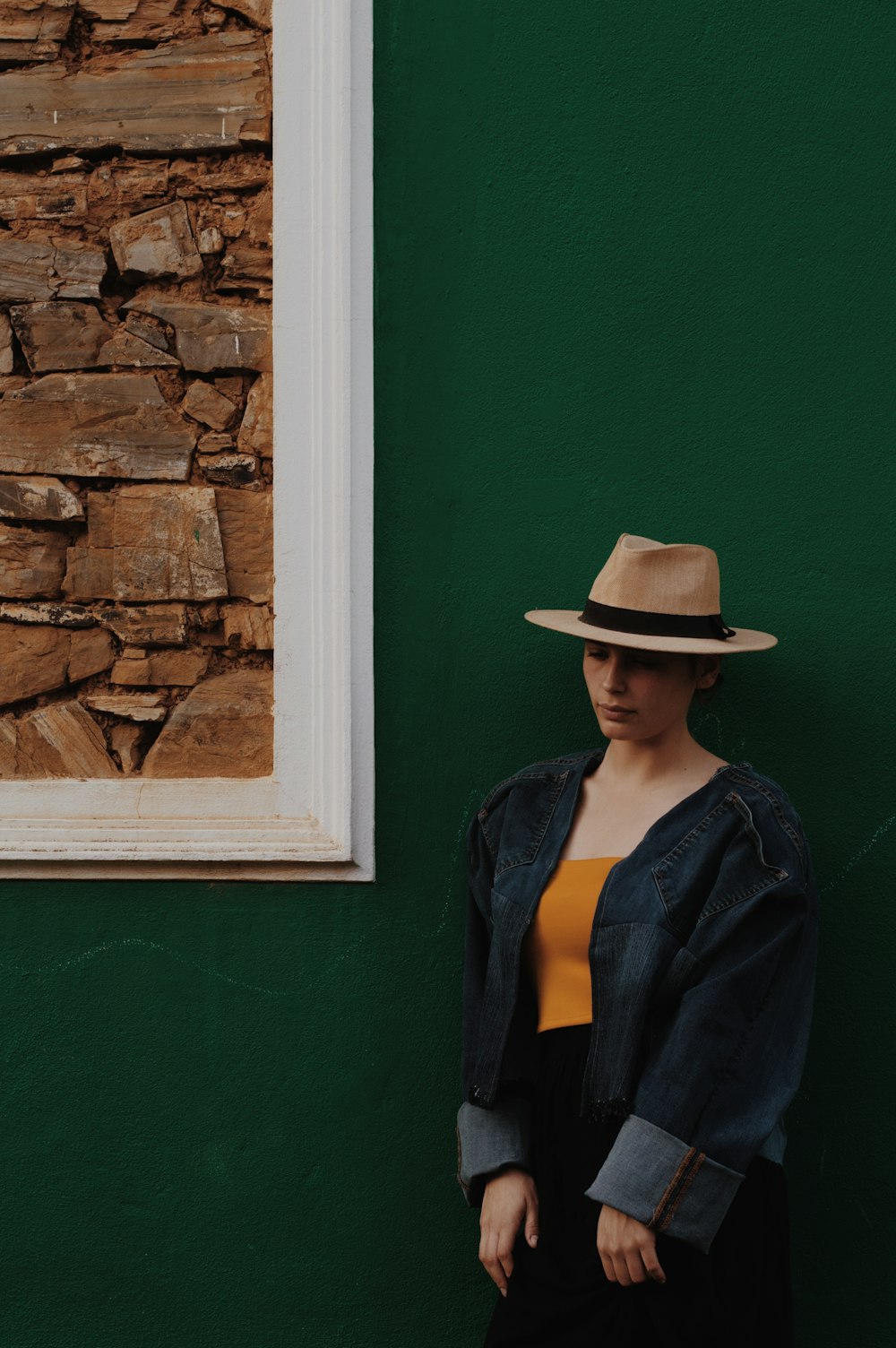 a woman in a hat leaning against a green wall