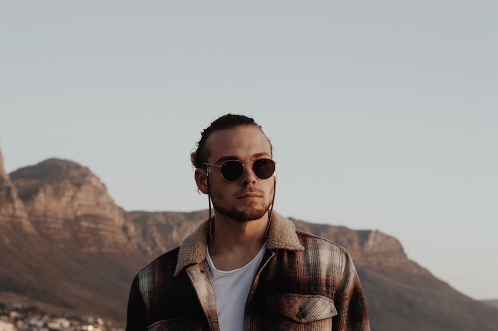 a man wearing sunglasses standing in front of a mountain