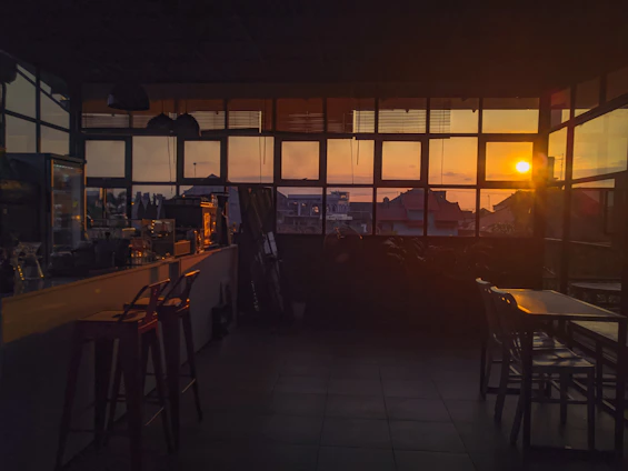 A cozy cafe interior at dusk with warm orange lighting and modern dark-themed decor.