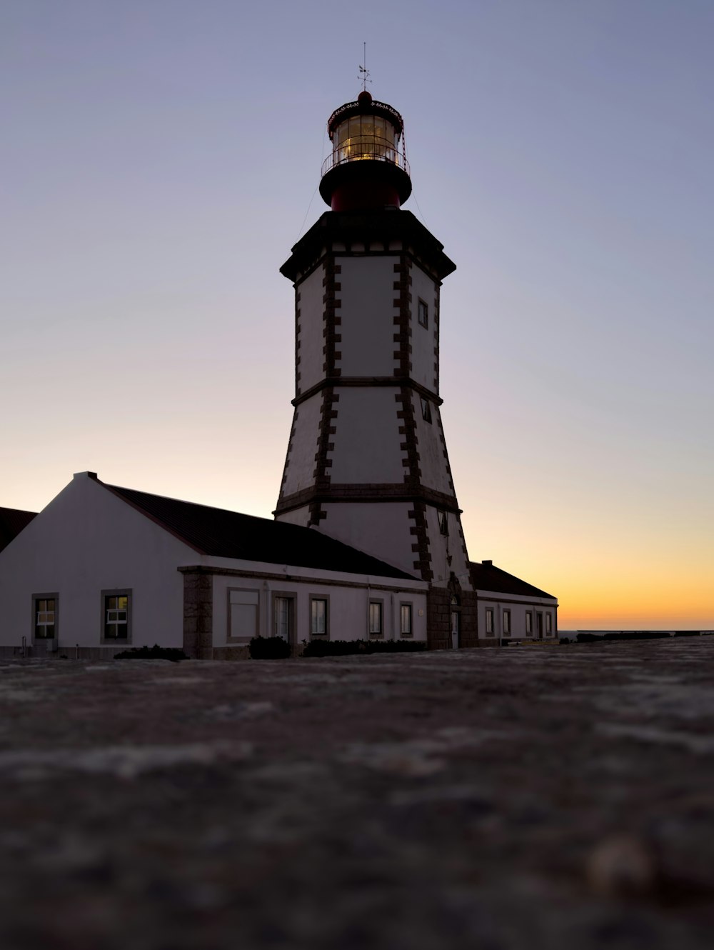 a white and black lighthouse with a sunset in the background