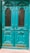 A pair of ornate teal double doors featuring intricate wooden carvings and decorative molding. The doors have metal grid windows and brass handles, adding to the classic design.
