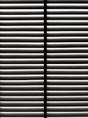 Horizontal blinds partially open with light filtering through the slats, casting striped shadows and creating a geometric pattern.