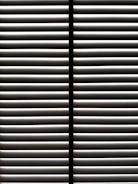 Horizontal blinds partially open with light filtering through the slats, casting striped shadows and creating a geometric pattern.