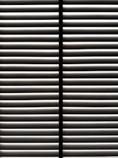 Horizontal blinds partially open with light filtering through the slats, casting striped shadows and creating a geometric pattern.