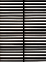 Horizontal blinds partially open with light filtering through the slats, casting striped shadows and creating a geometric pattern.