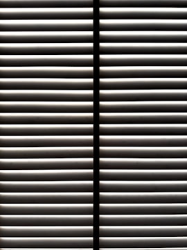 Horizontal blinds partially open with light filtering through the slats, casting striped shadows and creating a geometric pattern.