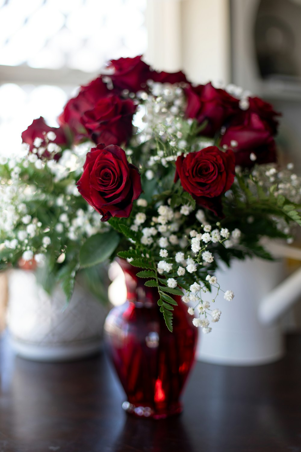 a red vase filled with red roses on top of a table
