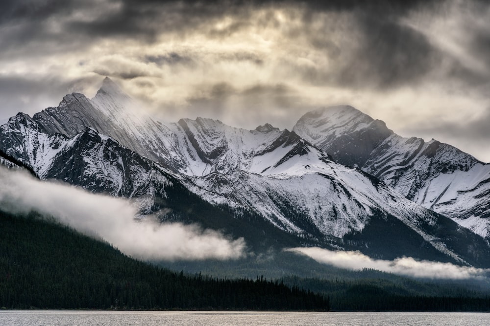 a mountain range covered in snow under a cloudy sky