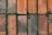 Several rectangular bricks arranged in a grid pattern with a rough surface. The bricks show signs of wear and have various shades of orange and brown. Small patches of moss and dirt are visible, along with a few fallen leaves scattered across the surface.