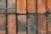 Several rectangular bricks arranged in a grid pattern with a rough surface. The bricks show signs of wear and have various shades of orange and brown. Small patches of moss and dirt are visible, along with a few fallen leaves scattered across the surface.