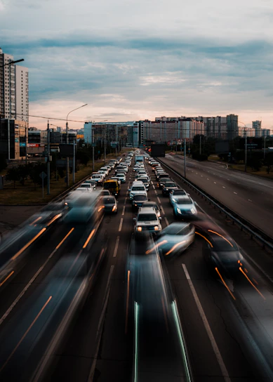 A busy city street clogged with cars emitting visible exhaust fumes under a gray sky.