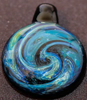 Shimmering galaxy resin pendant glowing softly against a dark fabric background