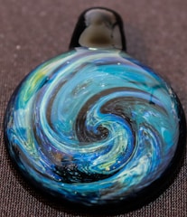 Close-up of a handcrafted epoxy resin pendant with swirling blue and white patterns.