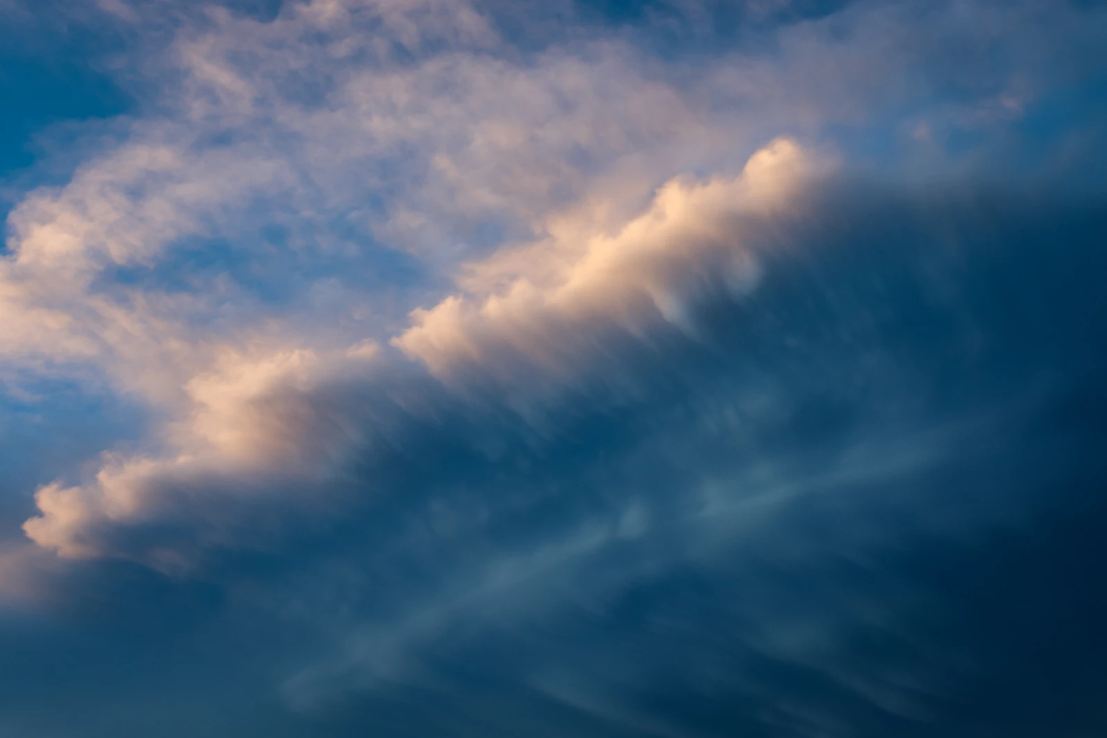 A small aircraft flying through a wide cloudy sky over open prairie
