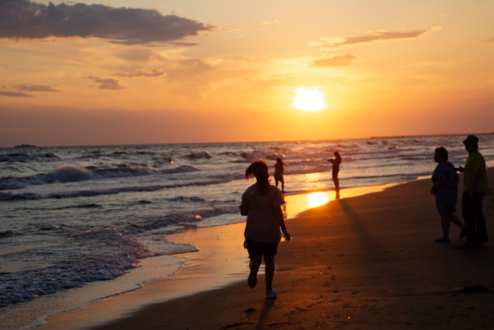 a group of people walking along a beach at sunset