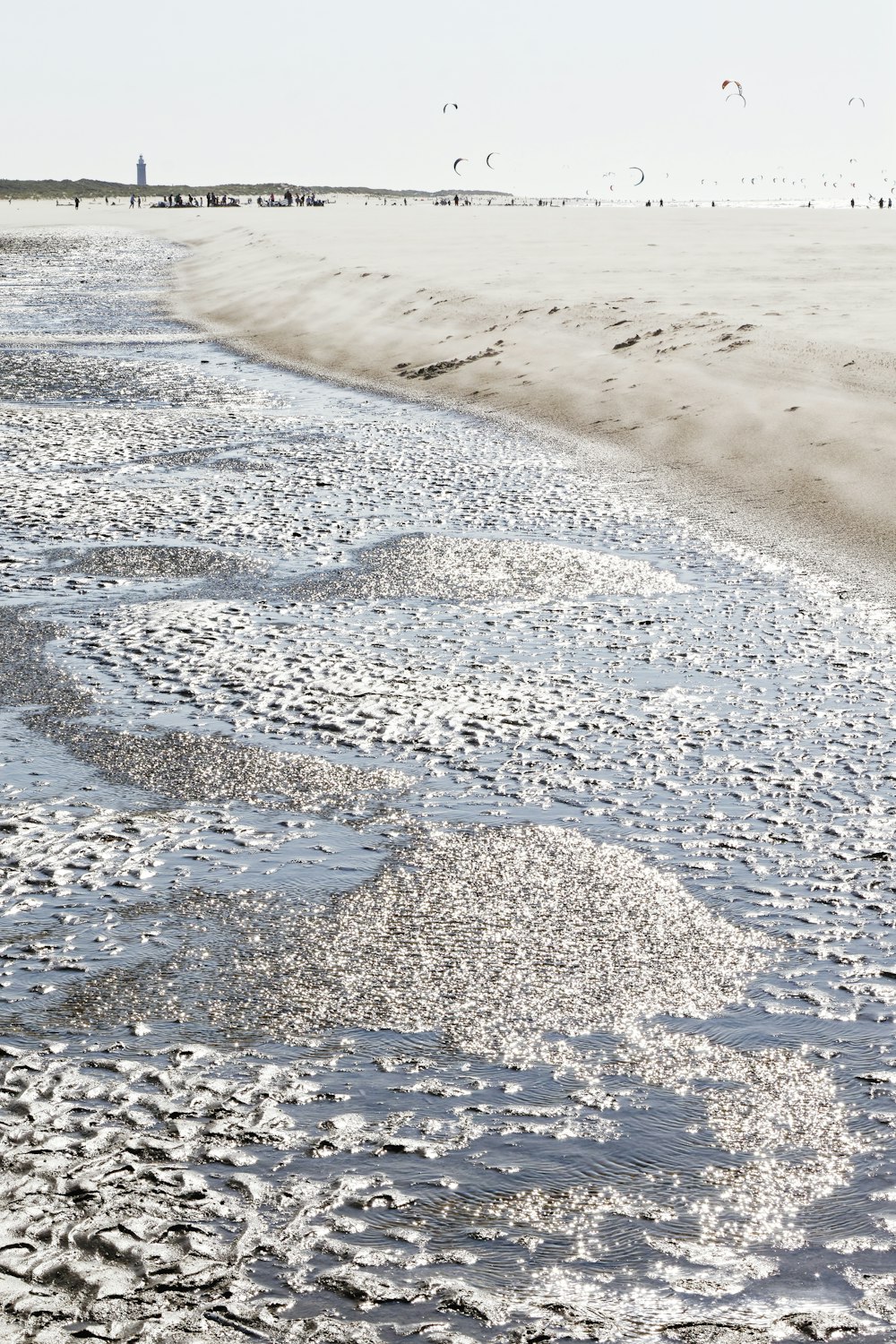 a sandy beach with waves coming in and people flying kites in the distance