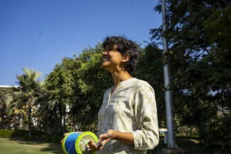 A child smiling while holding a colorful paper kite in a park.