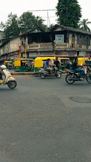 Tourists riding TVS Jupiter scooters past the vibrant street markets near Puri's temple area.