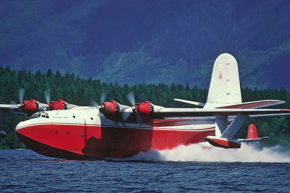 a red and white plane is flying over the water