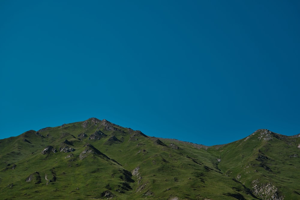 a green mountain with a blue sky in the background