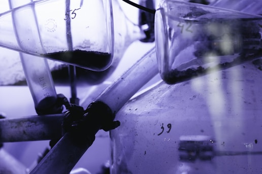 Several glass laboratory tubes and vessels with visible numbers and contents inside, possibly some kind of substance or powder. The setup appears to be part of a scientific or experimental apparatus with a bluish-purple tint dominating the scene.
