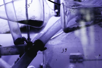 Several glass laboratory tubes and vessels with visible numbers and contents inside, possibly some kind of substance or powder. The setup appears to be part of a scientific or experimental apparatus with a bluish-purple tint dominating the scene.