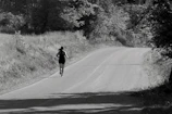 A person runs along a curved road surrounded by trees and grass, creating a sense of solitude and focus in a natural setting.
