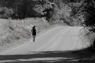 A person runs along a curved road surrounded by trees and grass, creating a sense of solitude and focus in a natural setting.