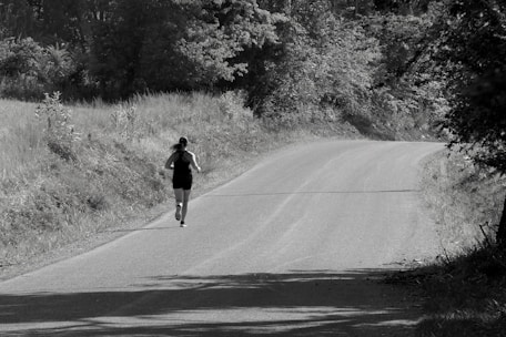 A person runs along a curved road surrounded by trees and grass, creating a sense of solitude and focus in a natural setting.
