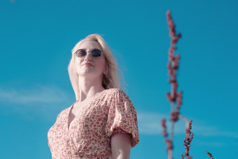 Une femme aux cheveux blonds et aux lunettes de soleil debout devant un ciel bleu