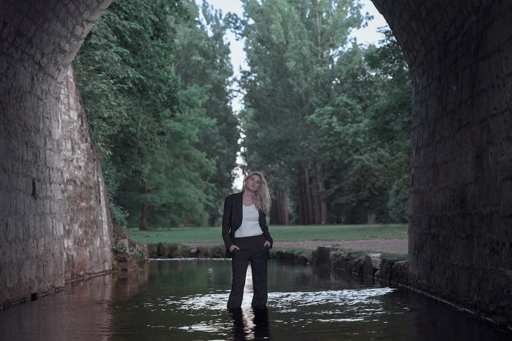 a woman standing in a river under a bridge