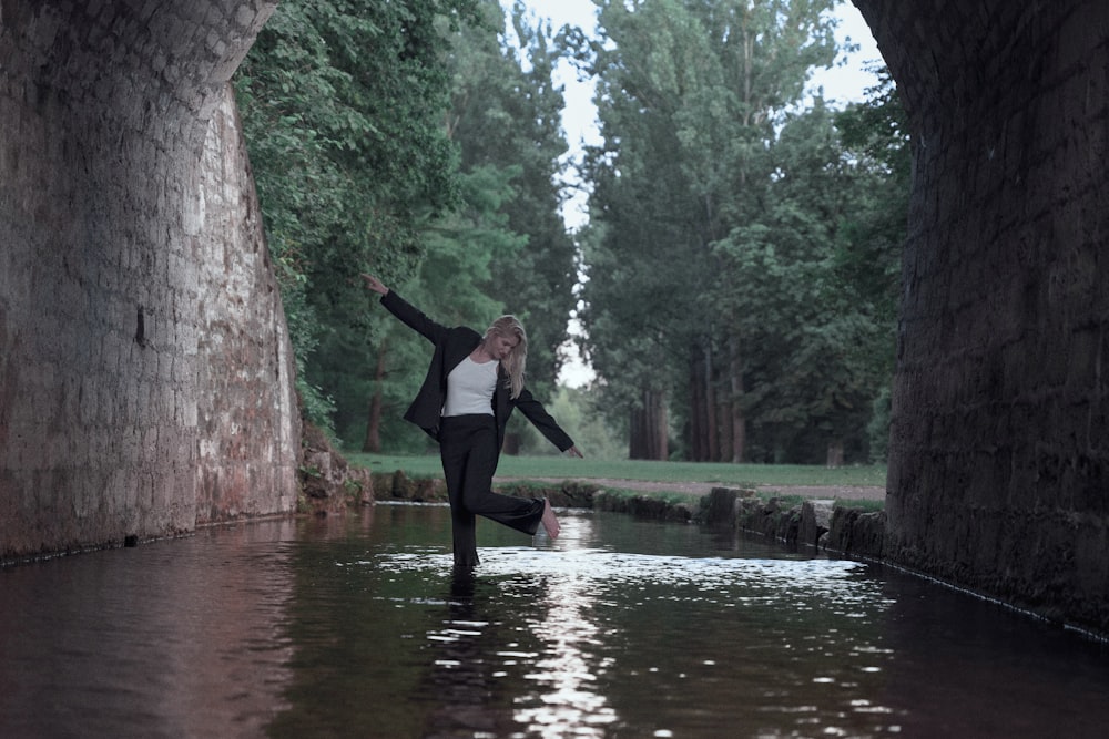 a woman in a white shirt and black pants is dancing in the water