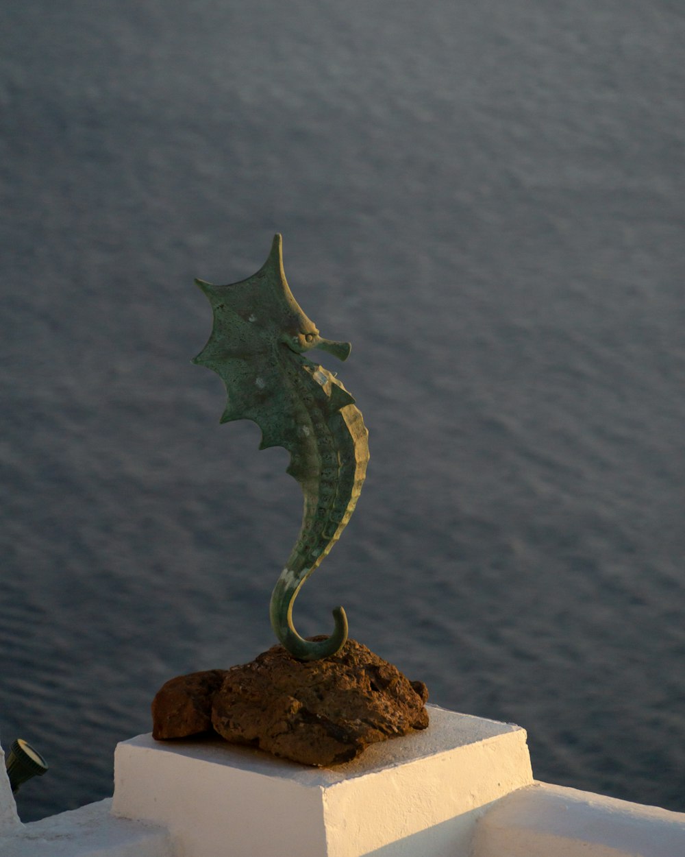 a metal seahorse on a rock near the water