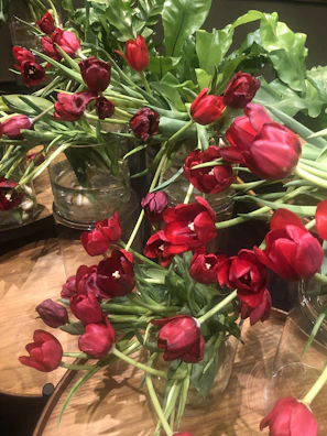 Bright tulips in assorted colors displayed in a modern glass container on a wooden table.