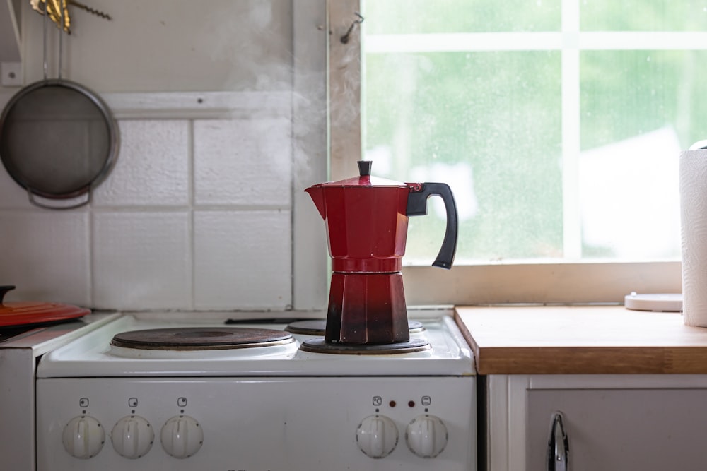 uma cafeteira vermelha sentada em cima de um fogão