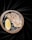 A single oyster on a half shell rests on a bed of ice inside a stone bowl, accompanied by a slice of lemon. The backdrop is a smooth, dark fabric that adds a touch of elegance to the composition.