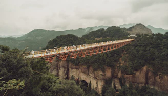 Hikers crossing a wooden bridge at Charyn Canyon with dramatic red cliffs all around.