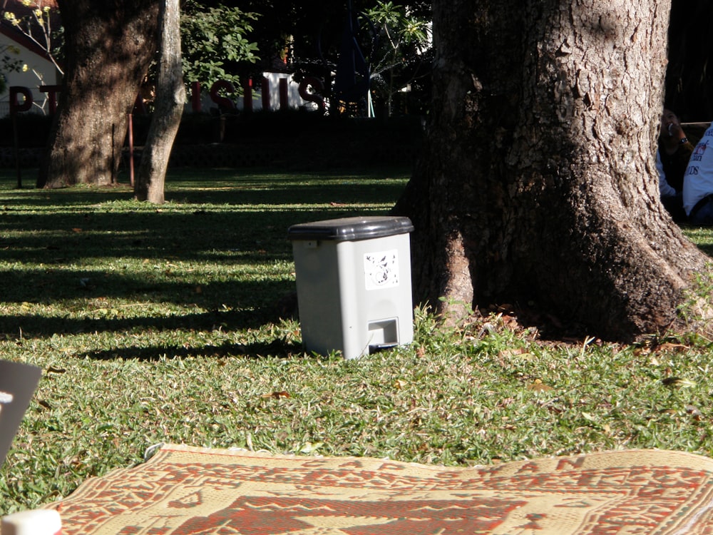 a trash can sitting in the grass next to a tree