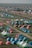 A large number of brightly colored tents are set up in a sprawling outdoor area, arranged in rows on green grass. There are paths between the tents and some canopy-covered seating areas with people gathered underneath. The area appears to be a campsite or festival setting with various colorful tents, possibly indicating a large event or gathering.