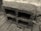 A concrete cinder block with rough texture positioned on a paved surface. The block has three large rectangular openings and is placed against a stone or concrete wall in an outdoor setting.