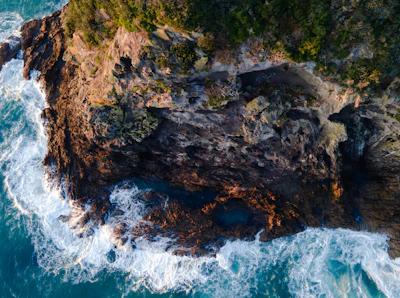 Aerial shot of rugged coastline with waves crashing against rocky cliffs.