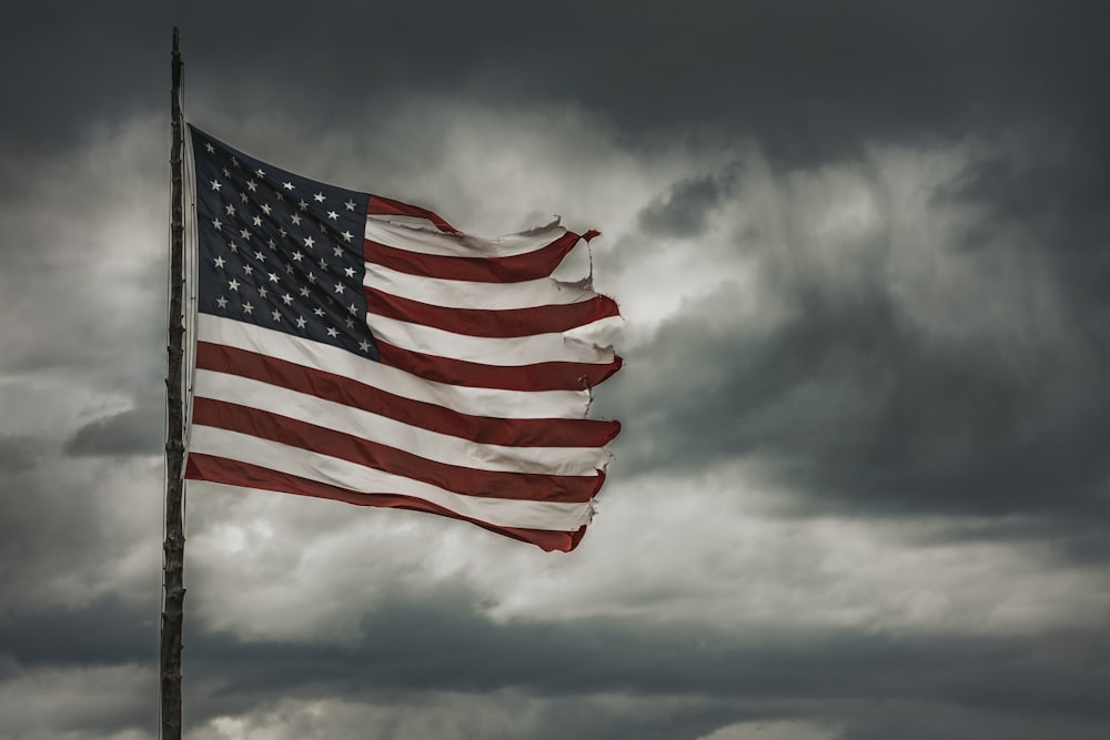 a large american flag flying in a cloudy sky