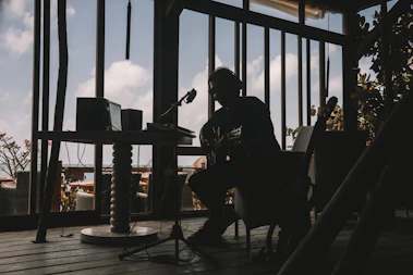 A candid portrait of Damon Perra playing guitar in a cozy, sunlit studio filled with vintage instruments.