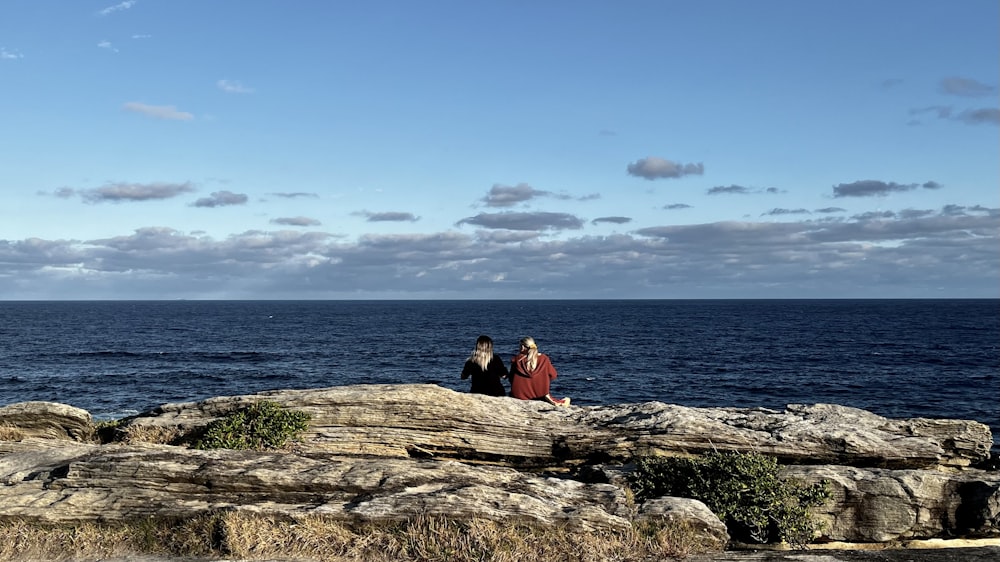 a couple of people sitting on top of a rock near the ocean